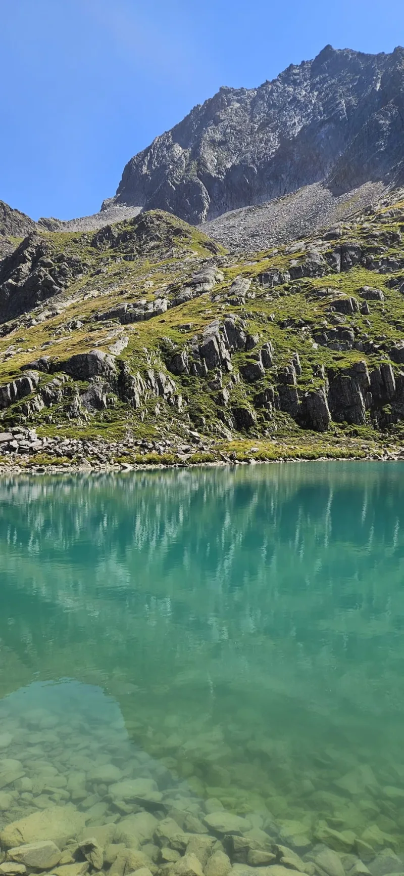 Klarer türkisfarbener Bergsee unter einem felsigen Gipfel